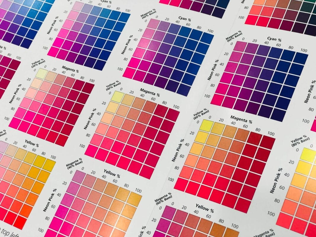 Close-up of color calibration charts for digital printing, showing a range of color swatches with percentages of cyan, magenta, yellow, and neon pink inks.