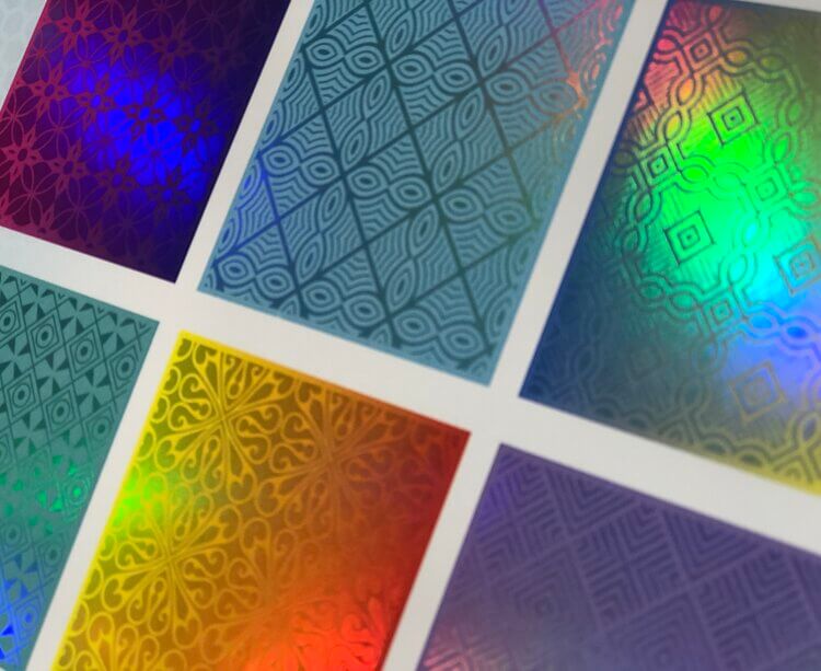 A close-up of various patterned samples showcasing vibrant, iridescent, and holographic foil effects achievable with digital printing, reflecting a rainbow of colors.