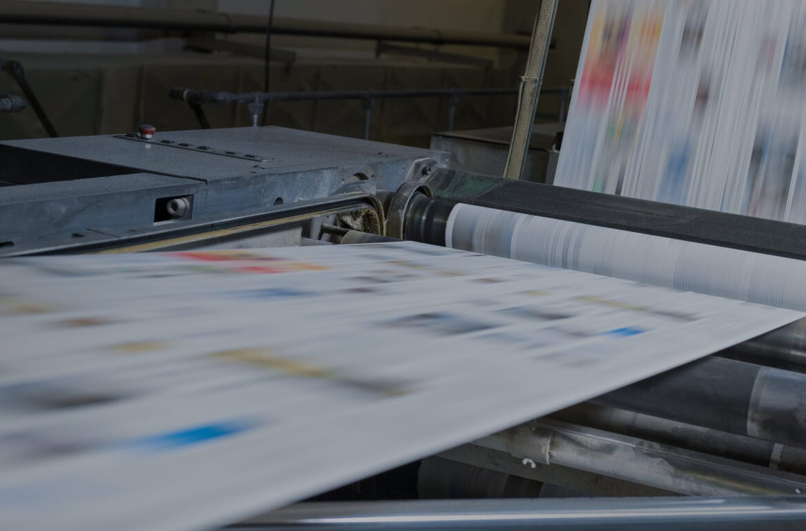 Close-up of a large industrial printing press in operation, with paper moving at high speed through the rollers, creating motion blur.