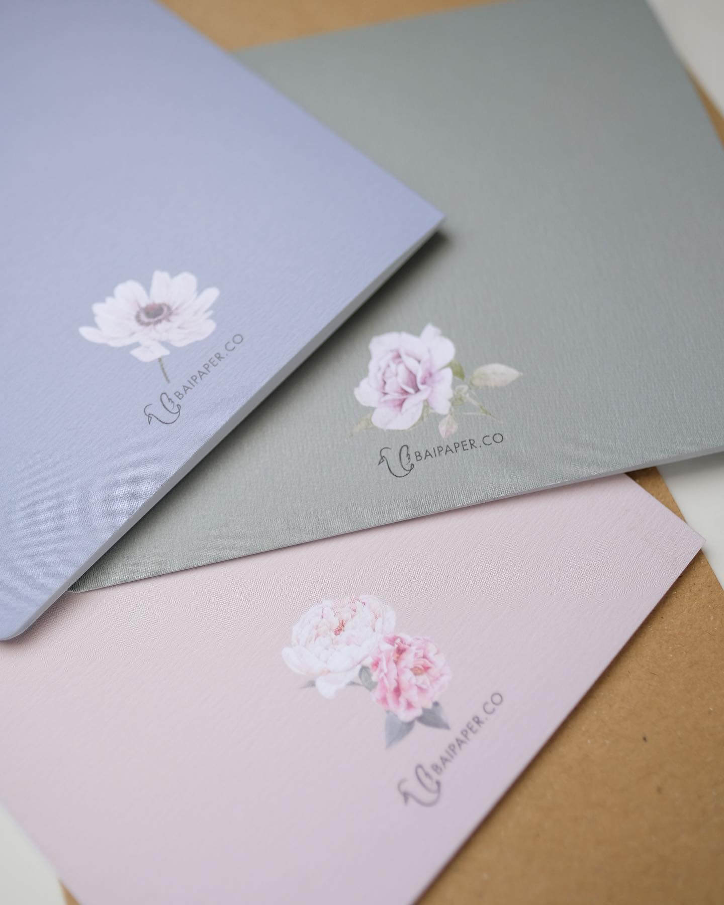 branded-notebooks-baipaper-collection A trio of sophisticated, branded notebooks in dusty blue, sage green, and pastel pink. Each cover is adorned with a unique floral print and the BAIPAPER.CO logo.