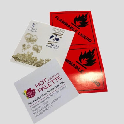 A variety of custom-printed stickers and labels, including red 'Flammable Liquid' warning labels, a corporate anniversary sticker with gold foil, and a business contact label.