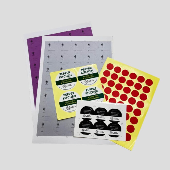 Several sample sheets of die-cut stickers and labels, displaying a variety of custom shapes from circular to branded designs for different applications.