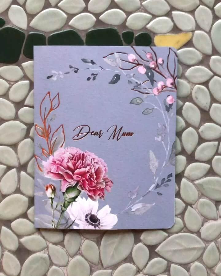 floral-foil-greeting-card-for-mum An artistic 'Dear Mum' greeting card with a lovely illustration of a carnation and foliage, accented with copper foil details, displayed on a textured, leaf-patterned tile background