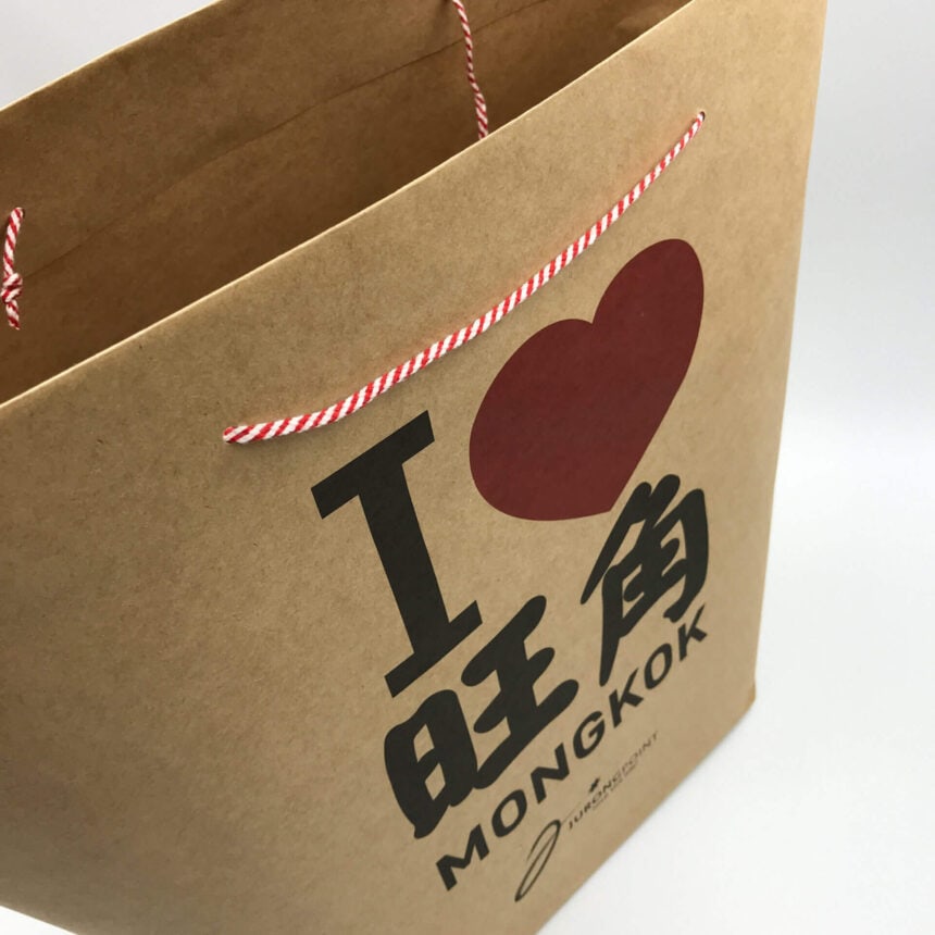 A close-up of a custom-printed brown kraft paper bag with red and white string handles