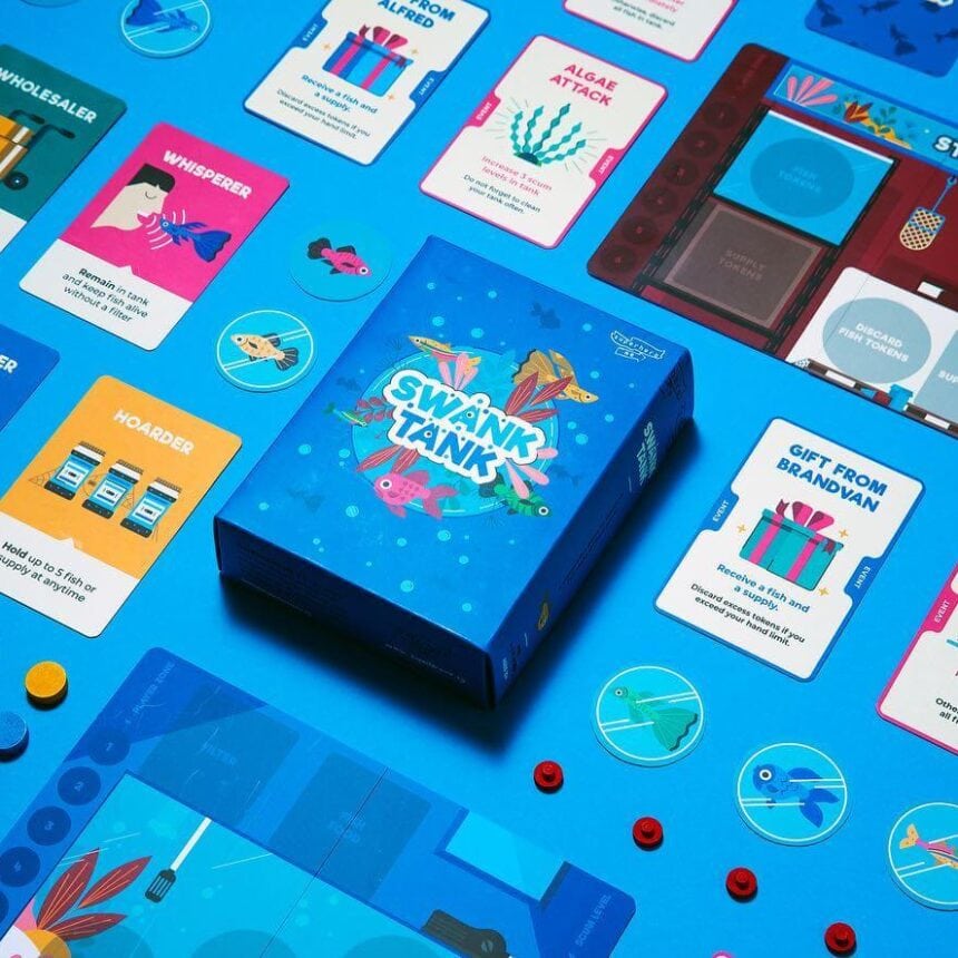 A flat lay of the 'Swank Tank' board game, showcasing the custom-printed box, colorful playing cards, and various game pieces