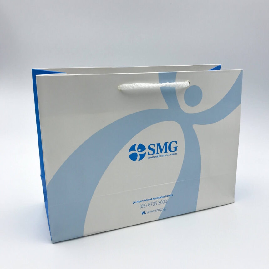 A custom-printed corporate paper bag for Singapore Medical Group (SMG), featuring their blue logo on a white background with rope handles and blue side gussets.