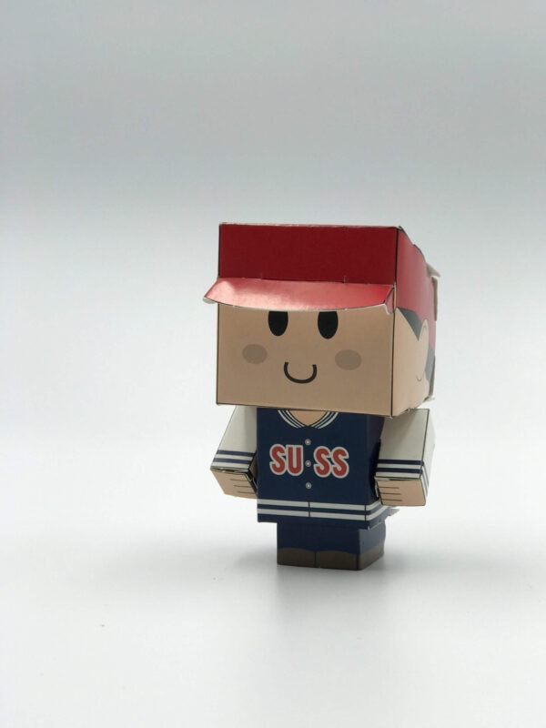 A custom-printed and die-cut papercraft toy of a character wearing a red cap and a blue 'SUSS' jacket, assembled and standing on a white background.