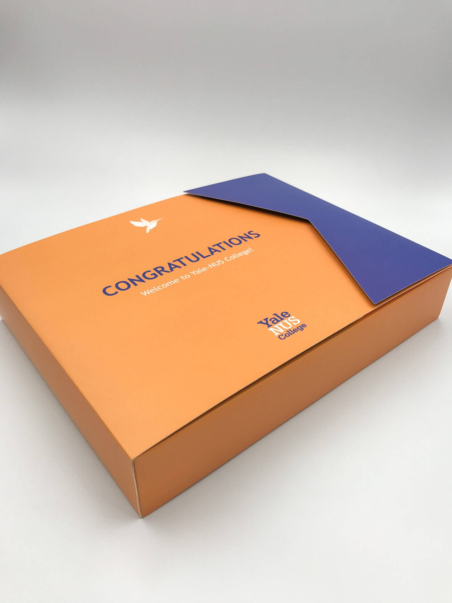 An elegant orange and blue custom presentation box for Yale-NUS College, featuring a unique die-cut flap and a 'Congratulations' welcome message.