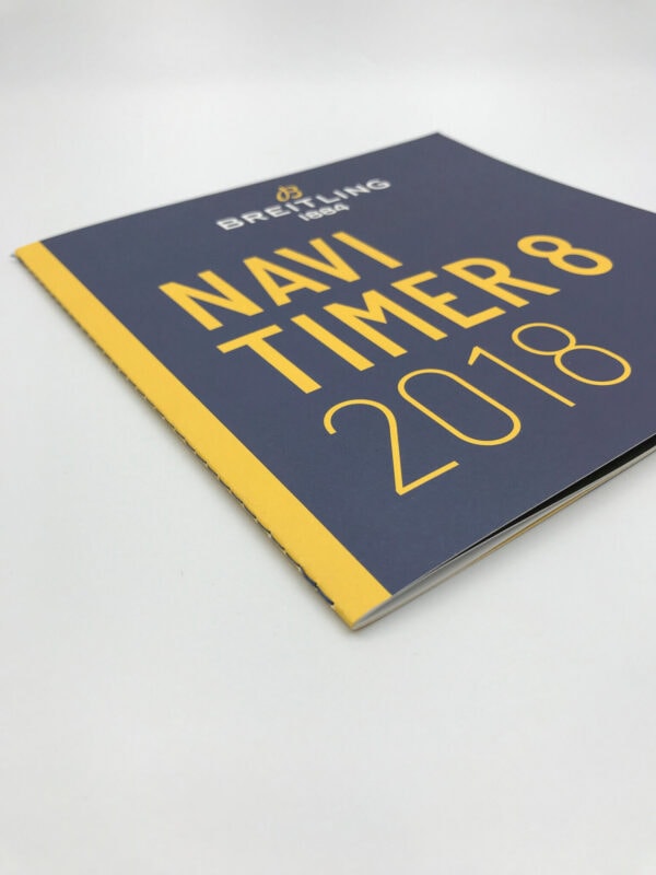 A high-quality, custom-printed product brochure for Breitling watches, with a striking dark blue and yellow cover design for the Navitimer 8 2018 model.