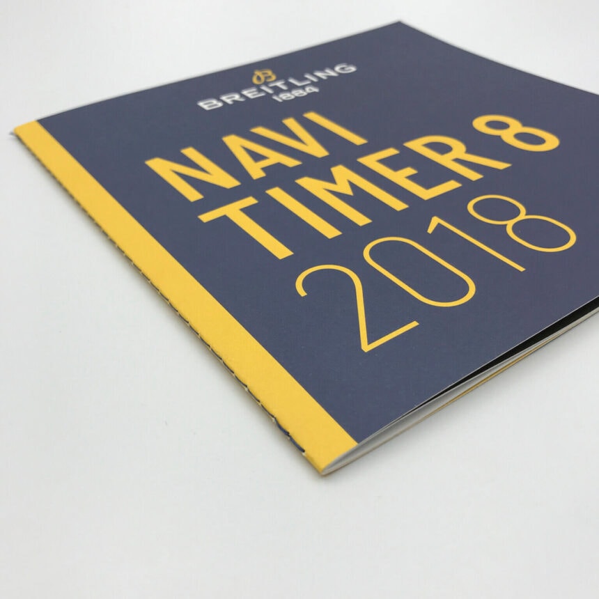 A high-quality, custom-printed product brochure for Breitling watches, with a striking dark blue and yellow cover design for the Navitimer 8 2018 model.