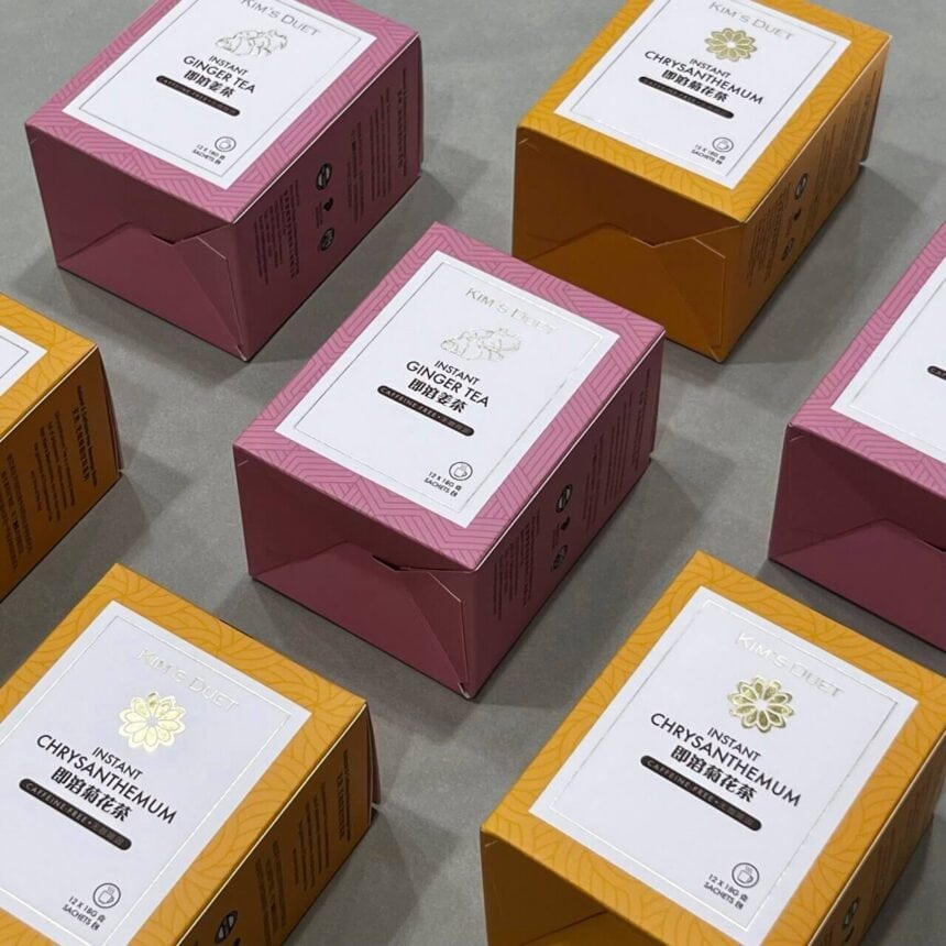 An arrangement of custom-printed boxes for Kim's Duet Instant Ginger Tea and Instant Chrysanthemum tea, showcasing the elegant pink and yellow product packaging with foil details.