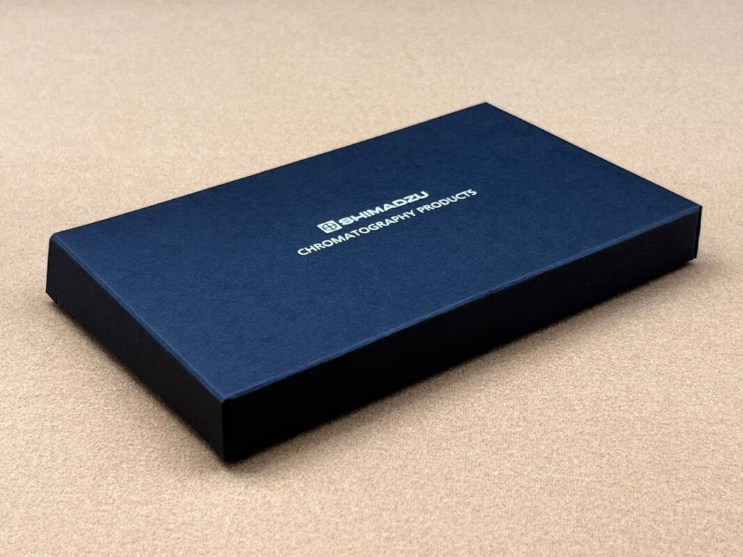 An elegant and minimalist black rigid box for Shimadzu Chromatography Products, featuring a clean design and a silver foil stamped logo on a textured surface.