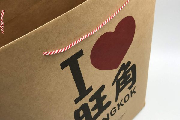 A close-up of a custom-printed brown kraft paper bag with red and white string handles