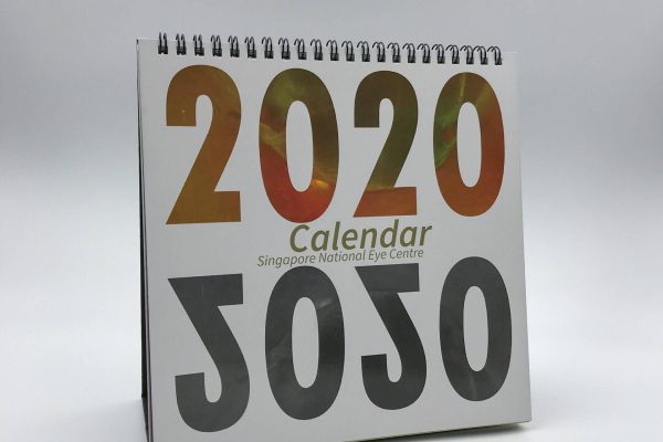 A custom-printed 2020 desk calendar for the Singapore National Eye Centre, featuring a bold design and standing upright with its wire-o binding