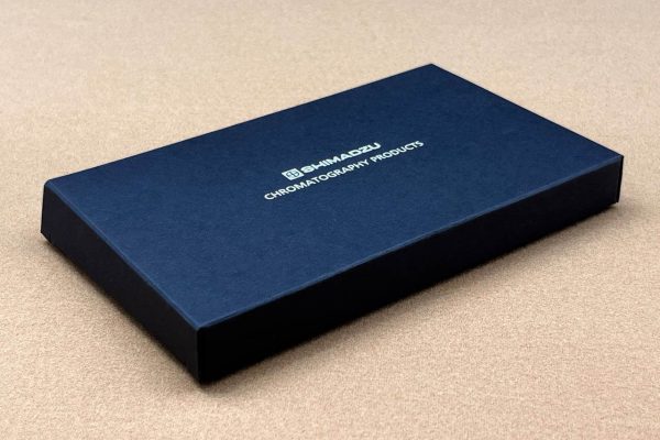 An elegant and minimalist black rigid box for Shimadzu Chromatography Products, featuring a clean design and a silver foil stamped logo on a textured surface.